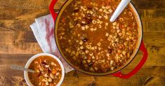 a red pot filled with soup next to a white bowl on top of a wooden table