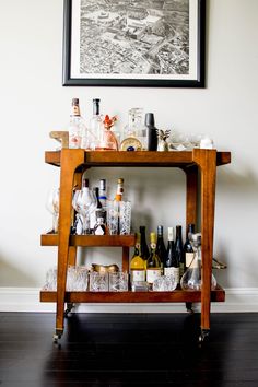 a wooden bar cart filled with bottles and glasses on top of a hard wood floor