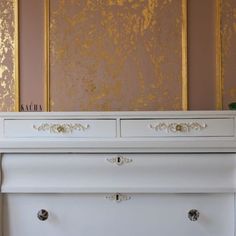 a white dresser sitting in front of a wall with gold paint on it's walls