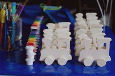 several plastic toy cars are lined up on a blue table with markers, pens and pencils