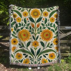 a quilt with sunflowers on it hanging from a wooden fence in front of some trees