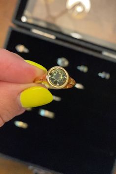 a woman's hand holding a yellow ring with a green diamond on it, in front of a jewelry box