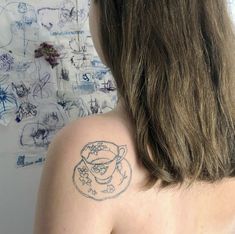 the back of a woman's shoulder with a tattoo on her left arm and a cup of coffee in front of it