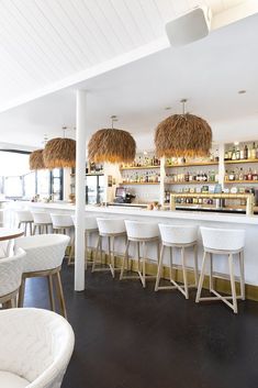 an empty bar with white chairs and straw lamps