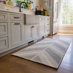 a kitchen with white cabinets and wooden flooring next to a large rug on the floor