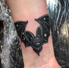 a small bat tattoo on the wrist is shown in black and grey colors, with stars around it