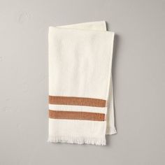 a white towel with brown stripes hanging on a wall in front of a gray wall