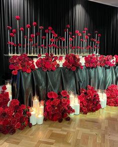 red flowers and candles are arranged on the floor in front of a black curtained backdrop