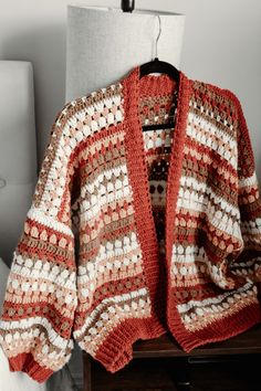 a red and white crocheted cardigan sitting on top of a wooden table