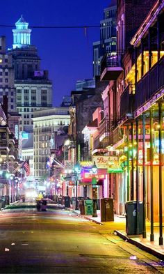 an empty city street at night with buildings lit up in the background and cars driving down the road