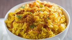 a white bowl filled with yellow rice on top of a table