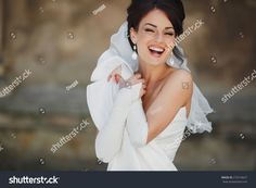 a woman in white wedding dress smiling and holding her coat over her head with both hands