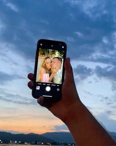 a hand holding up a cell phone with a photo on the screen in front of a sunset