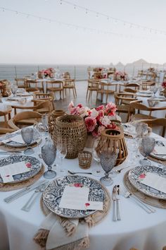 a table set with place settings and flowers on top of it, next to the ocean