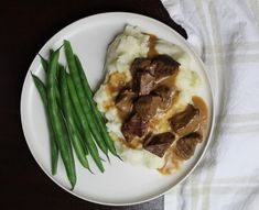 a white plate topped with mashed potatoes covered in gravy and green beans