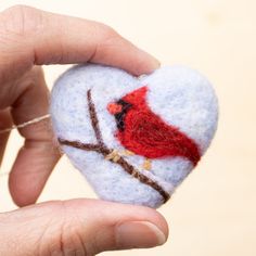 a hand holding a felt heart with a red bird on it