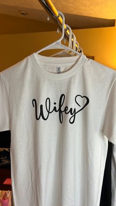 Get ready to rock your wedding with this stunning Wifey Tee! This T-shirt is perfect for any bride or wife-to-be who wants to show off her status in style. Made for women of all sizes, this white T-shirt comes with tags and features the word "Wifey" printed in bold letters, making it an ideal choice for any wedding ceremony or reception.  The tee is available in regular size and can be paired with any bottom of your choice, be it a skirt, jeans, or shorts. The bright white color of the T-shirt is perfect for any occasion, be it a formal or a casual event. Get ready to make a statement with this beautiful Wifey Tee and show off your love in style! White Short Sleeve Top For Bridal Shower, White Crew Neck Top For Bridal Shower, White Bridal T-shirt With Short Sleeves, White T-shirt For Bridal Shower Short Sleeve, White Short Sleeve T-shirt For Bridal Shower, White Fitted T-shirt For Bachelorette Party, White Short Sleeve Top For Wedding, Fitted White Top For Bridal Shower, White Fitted Top For Bridal Shower