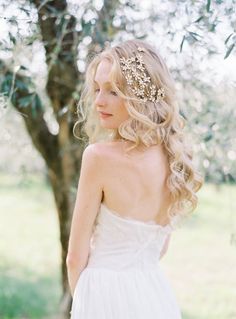 a woman in a white dress standing next to a tree wearing a headpiece with flowers on it