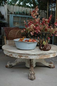 an old table with a bowl of fruit on it and some flowers in the background