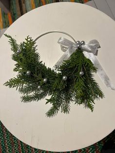 a christmas wreath on a white table with silver balls and ribbon hanging from it's center