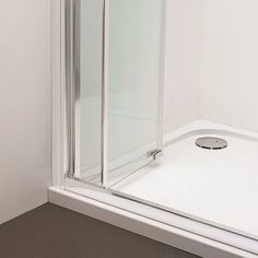 a bathroom with a glass shower door next to a white wall and brown flooring