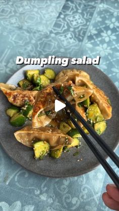 someone holding chopsticks over a plate of food with dumplings and sauce on it