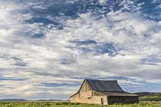 an old barn sitting in the middle of a green field under a cloudy blue sky