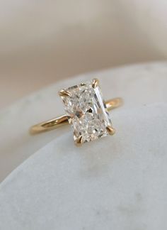 a yellow gold engagement ring with a princess cut diamond in the center, on a white marble surface