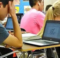 two students sitting at desks with their laptops open and one student has his head in his hands