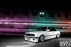 a white car parked in front of a tall building at night with colorful lights behind it