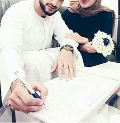 a man and woman sitting at a desk signing papers with pen in their hands while wearing hijabs