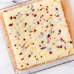 a square cake with white frosting and cranberries sitting on a cooling rack