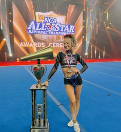 a cheerleader holding a trophy next to a trophy on a blue floor with lights in the background