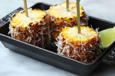 four pineapples with toothpicks in a black tray on a white table