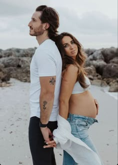 a pregnant woman standing next to a man on the beach