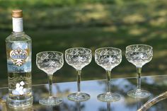 four wine glasses and a bottle sitting on a glass table with grass in the background