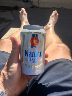 a person laying on the ground with their feet up holding a can of natural light beer