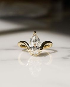 a yellow gold ring with a pear shaped diamond in the center, on a white surface