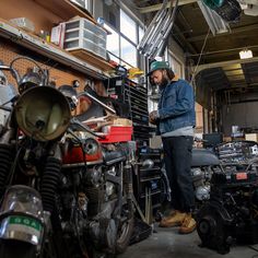 a man standing next to a motorcycle in a room filled with other motorcycles and parts