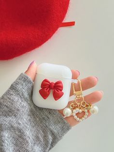 a hand holding an airpods case with a red bow on it and pearls hanging from the side