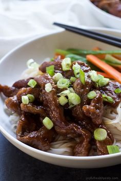 a white bowl filled with meat and noodles next to chopsticks on a table