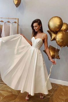 a woman in a white dress holding some gold balloons