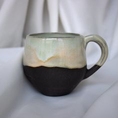 a black and white coffee cup sitting on top of a white cloth covered tablecloth