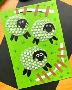 two sheep made out of green paper sitting on top of a black and white table