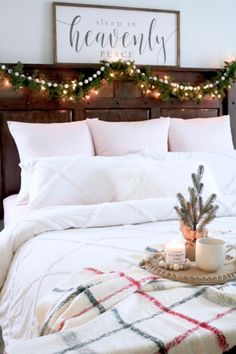 a white bed topped with pillows and blankets next to a wooden headboard covered in christmas lights