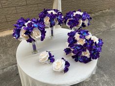 purple and white flowers are arranged in vases on a round table with a brick wall behind it