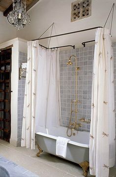 a bath tub sitting under a chandelier next to a white curtained wall