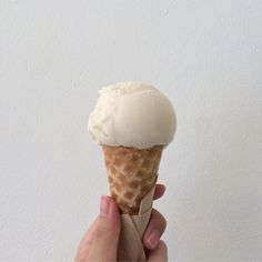 a hand holding an ice cream cone in front of a white wall with the top half eaten