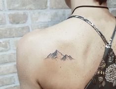 a woman with a mountain tattoo on her upper back shoulder and neck is standing in front of a brick wall