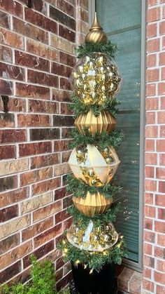 a tall christmas tree with gold ornaments on it in front of a brick wall and window